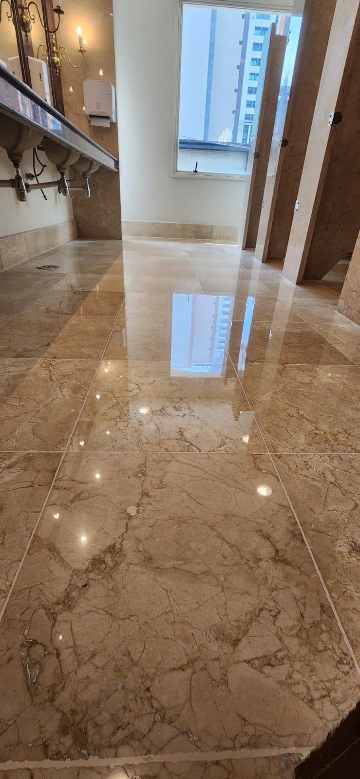 Banheiro corporativo com piso de mármore polido refletindo a luz natural